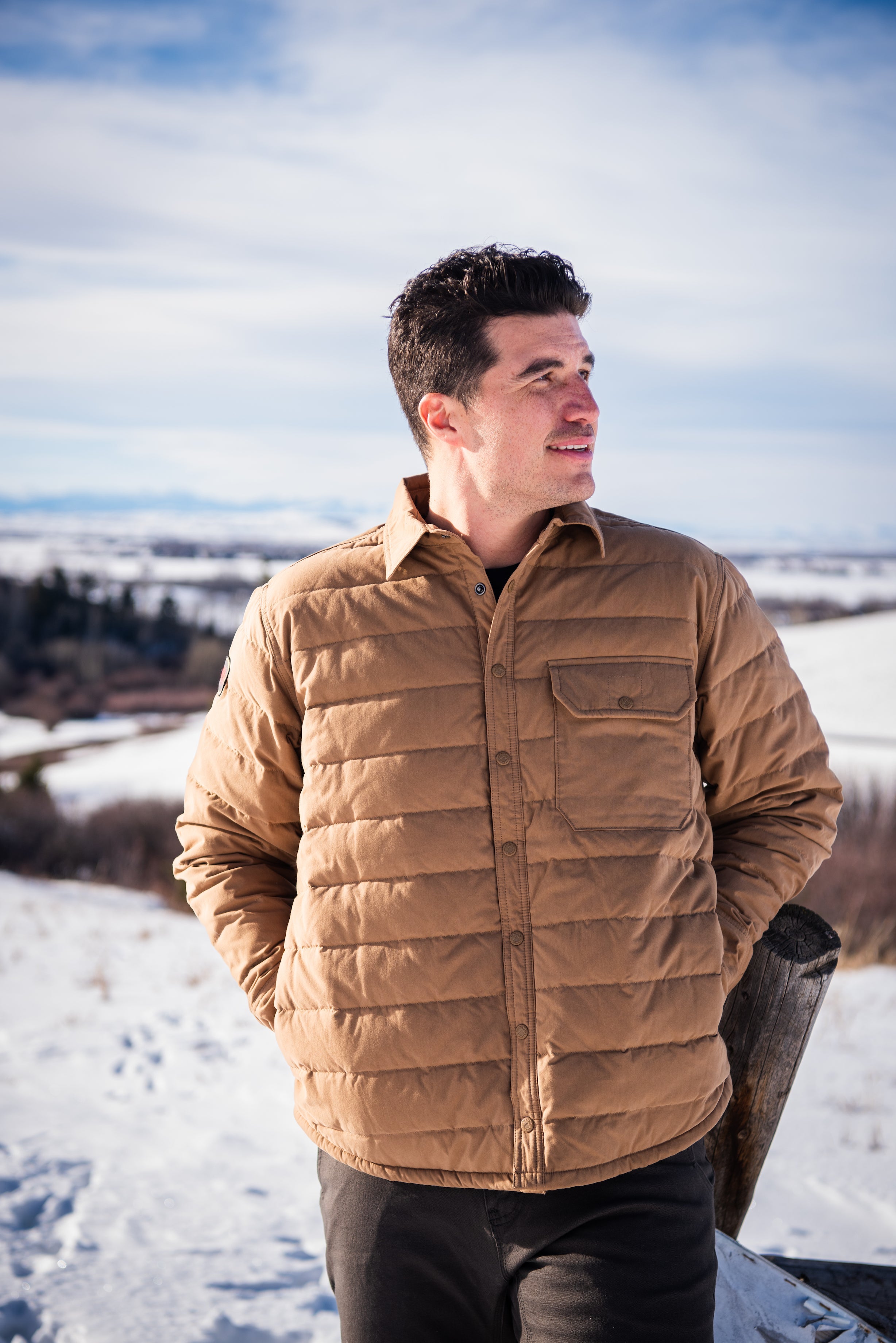 A man wears Pine Peak Down Shirtjac standing in the snow