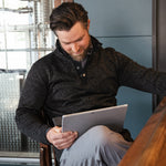 A man wears  Norris Pullover sitting at a chair and reading material