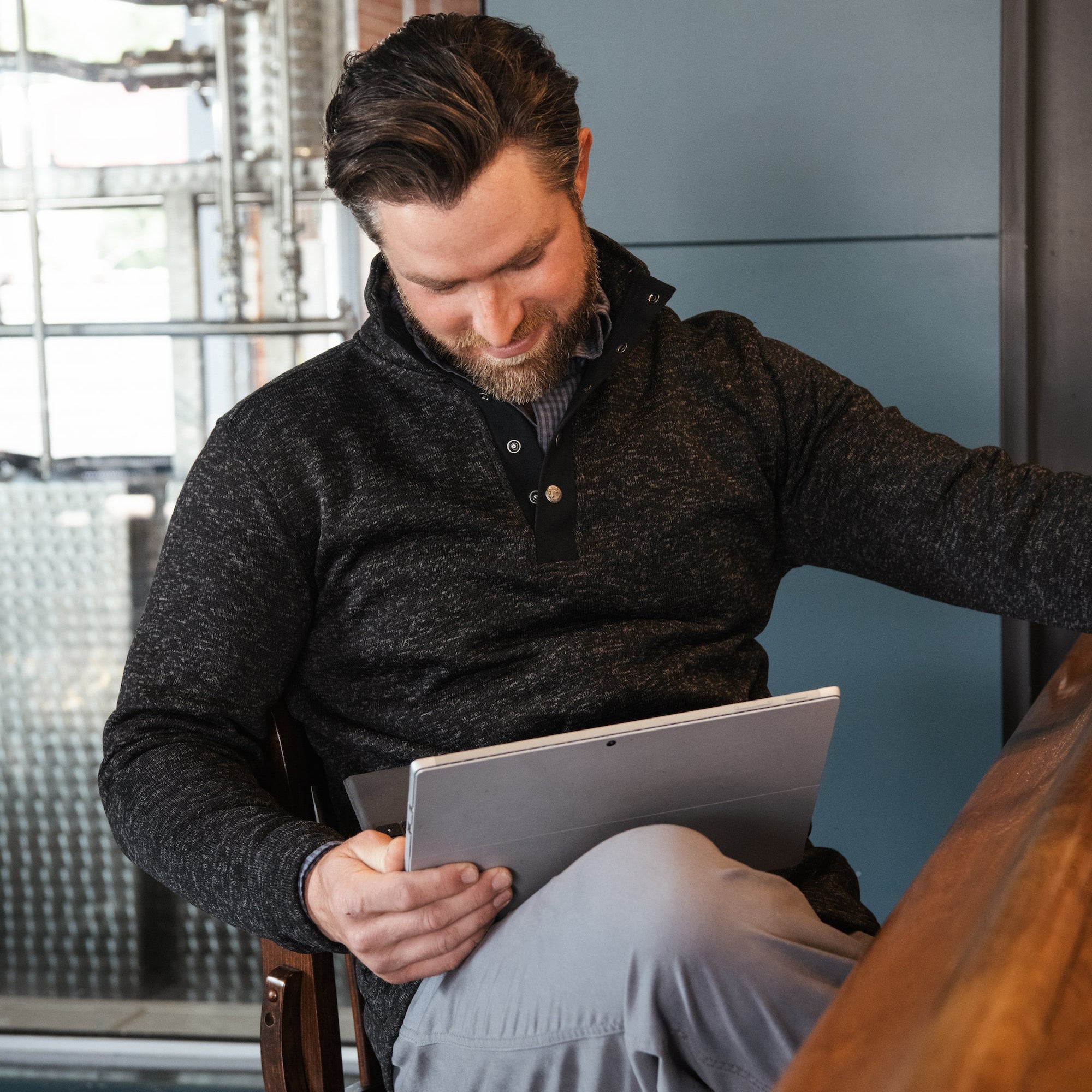 A man wears  Norris Pullover sitting at a chair and reading material