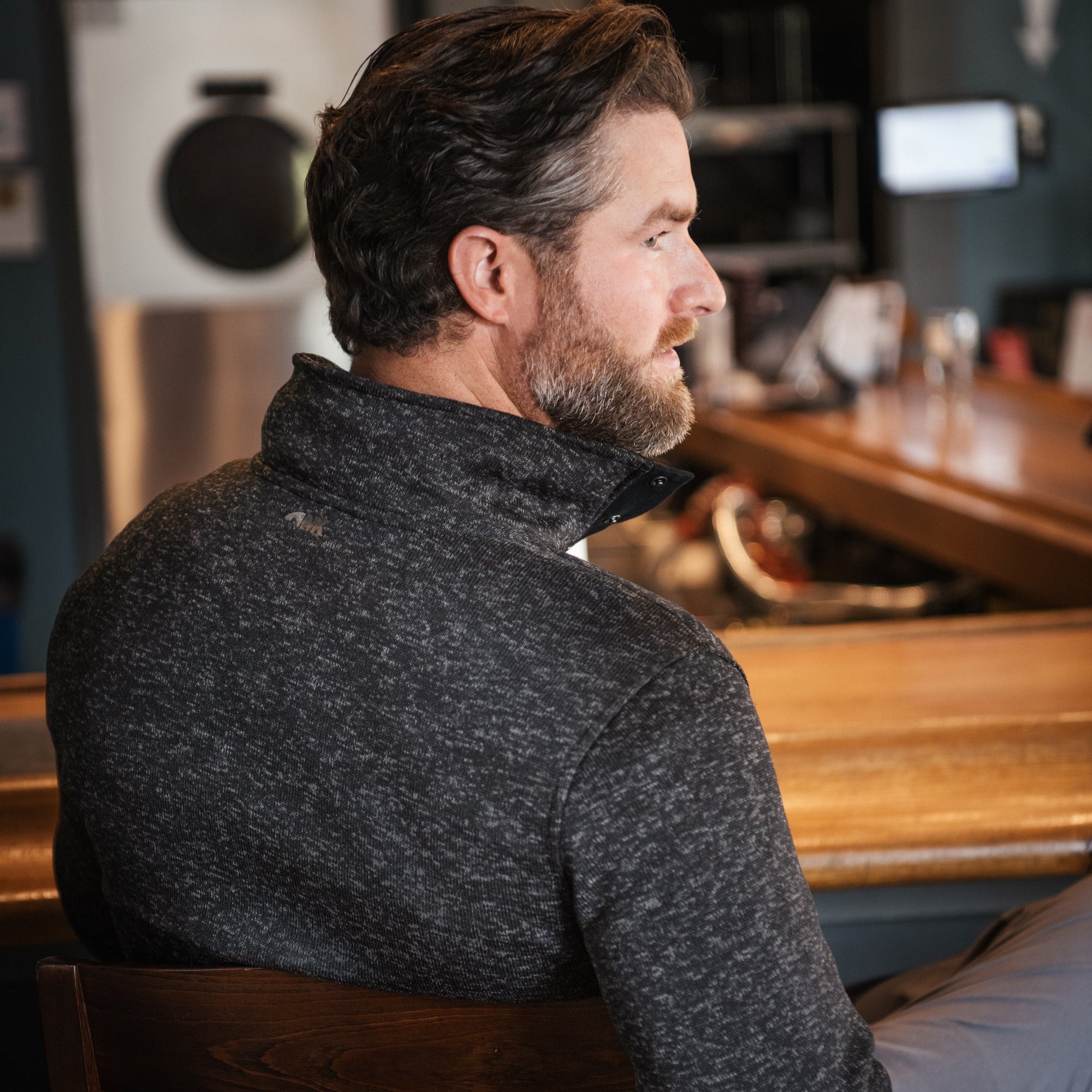 A man wears  Norris Pullover sitting at a chair and reading material