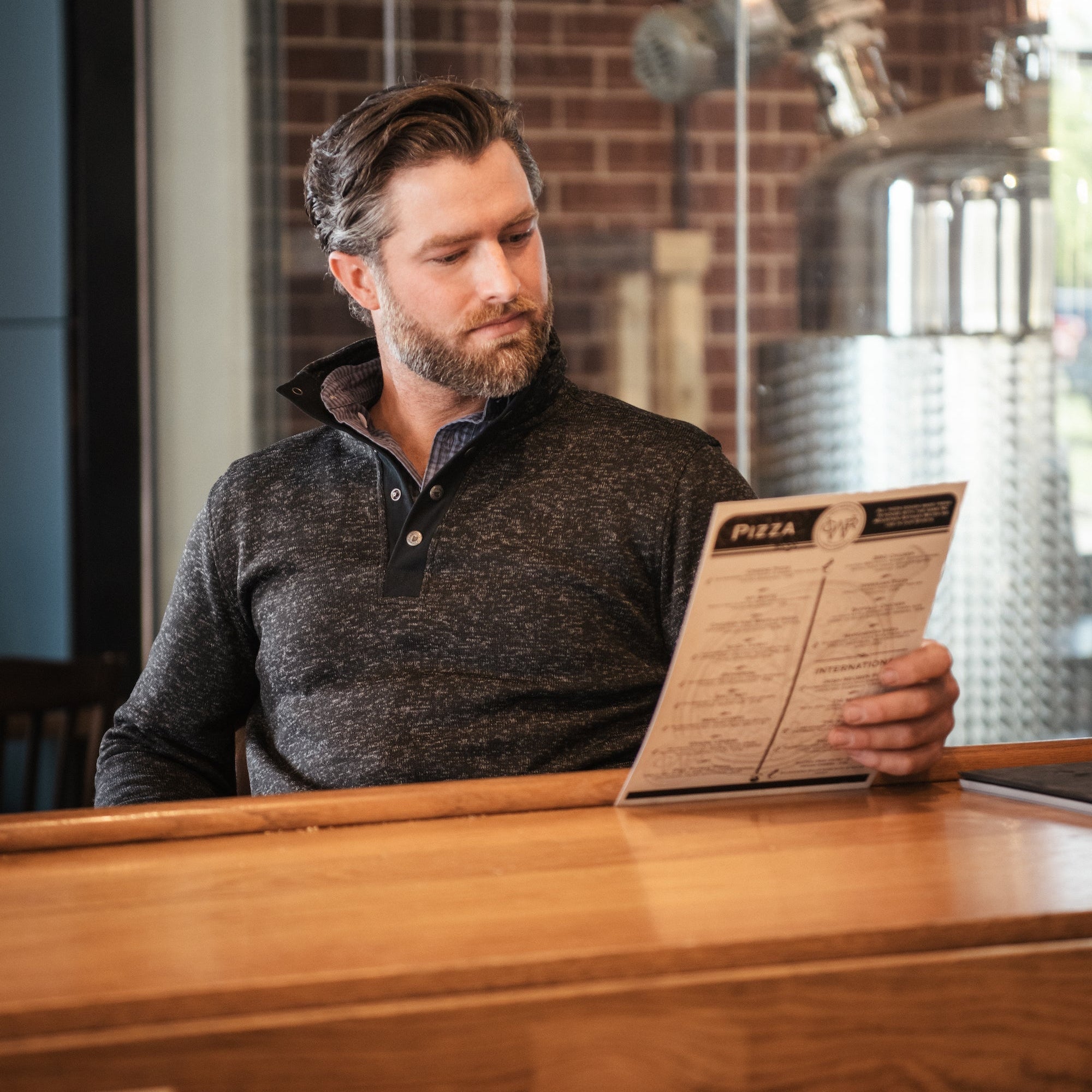 A man wears  Norris Pullover sitting at a chair and reading material