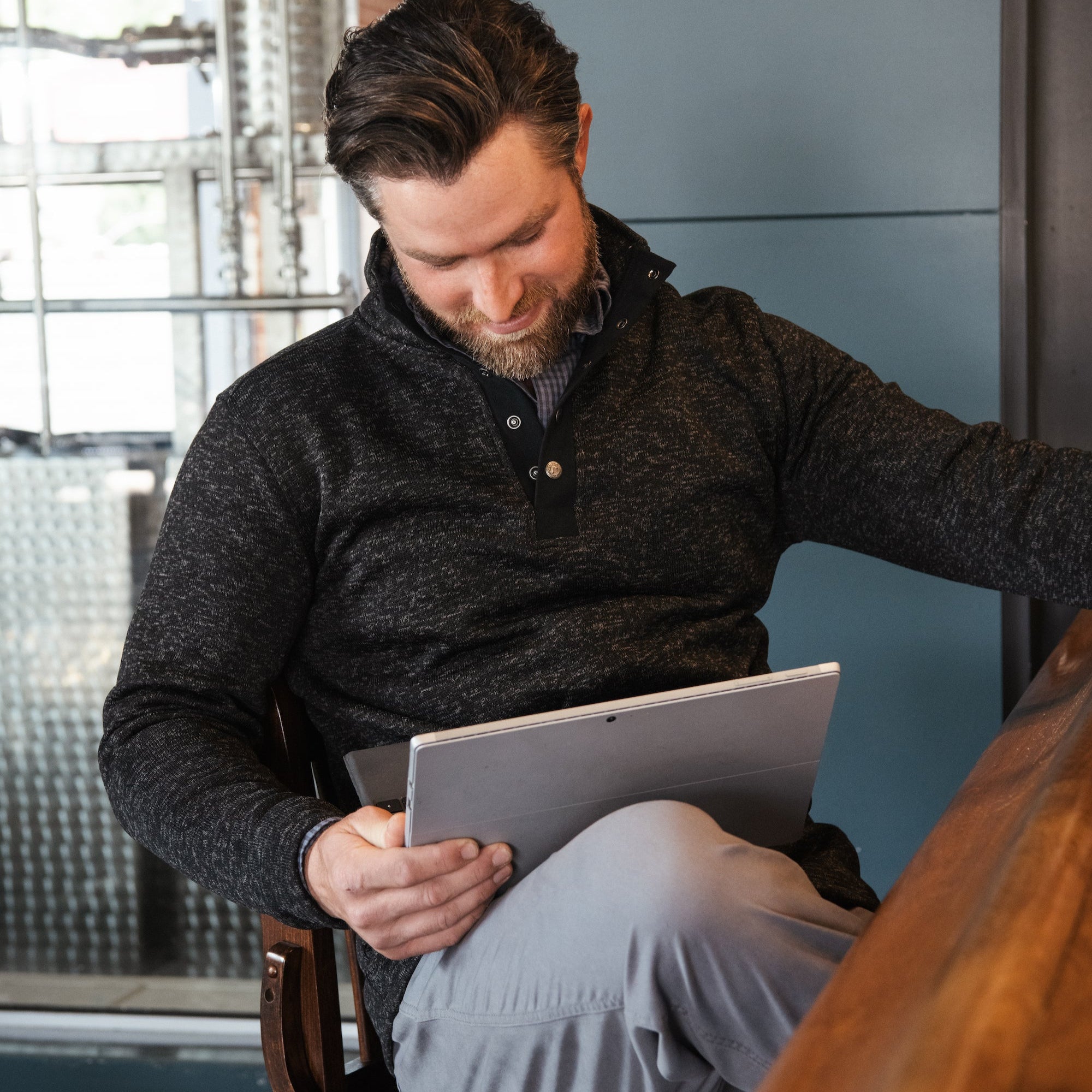 A man wears  Norris Pullover sitting at a chair and reading material